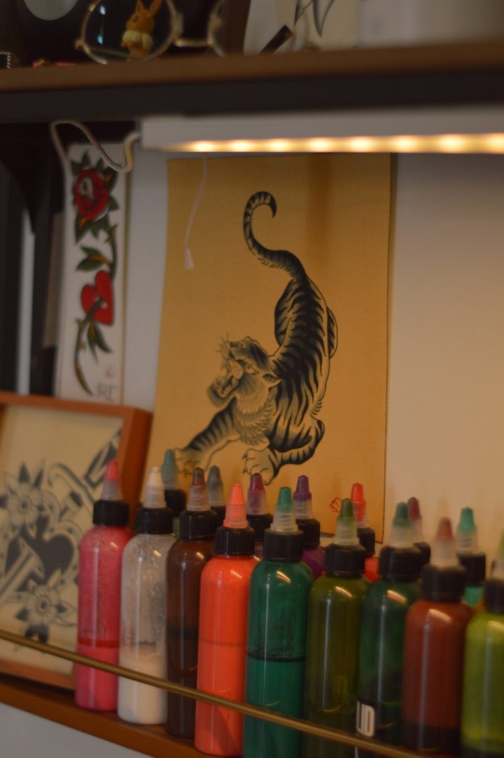 A shelf of ink bottles under a strip light, with tiger and rose flash pinned behind it.