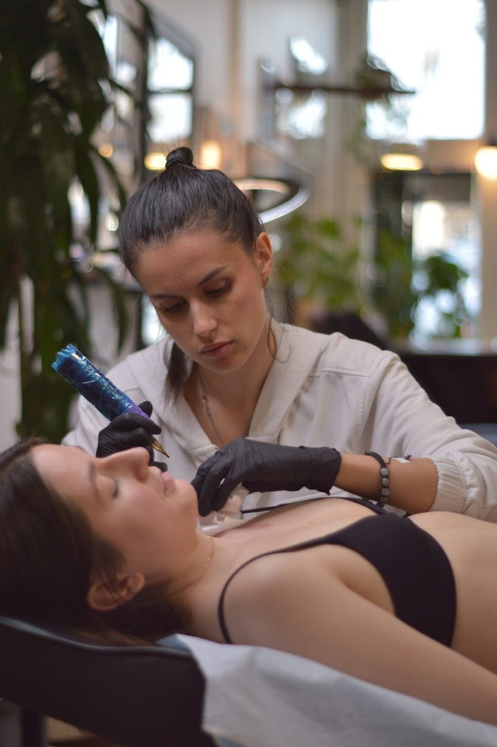 An artist tattooing a client's sternum in the shop's front window light.
