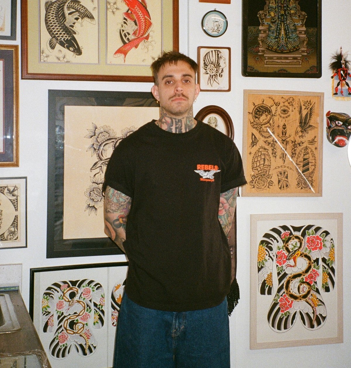 A tattooed man standing in La Rosa among framed koi paintings, flash sheets and a Japanese bodysuit painting.