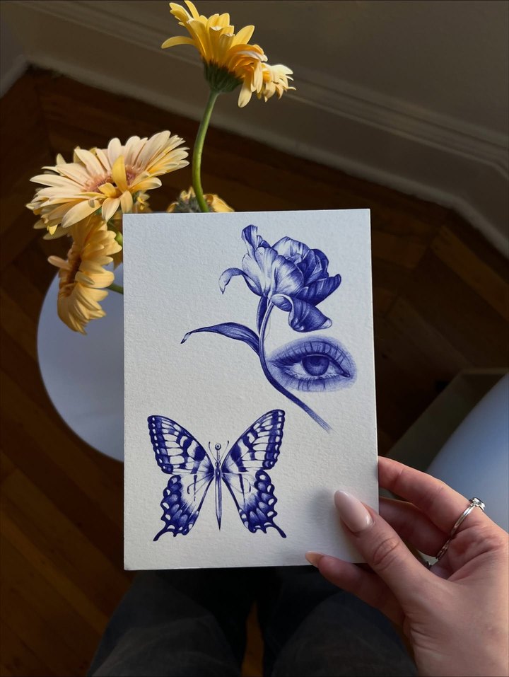 A blue ballpoint drawing of a tulip, an eye and a butterfly on paper.