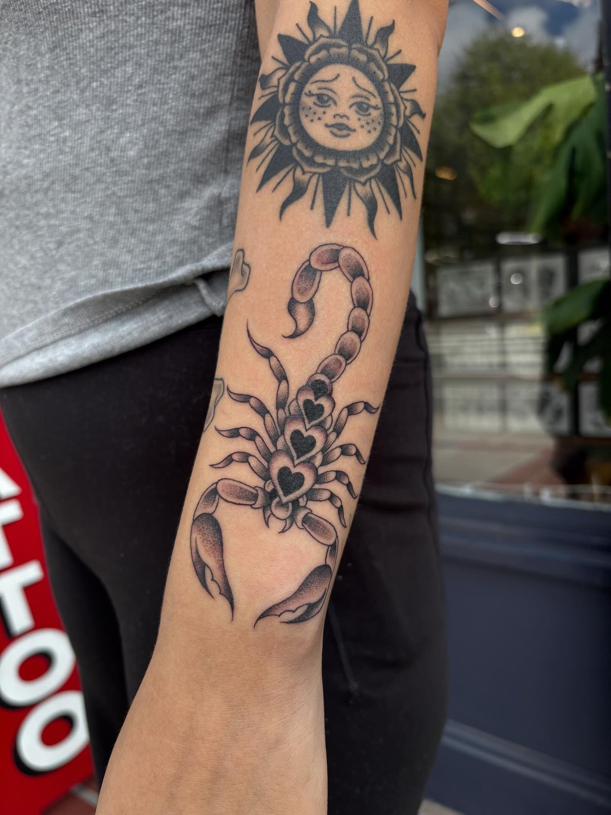 Un tatuaje tradicional de escorpion y sol ya curado en un antebrazo, frente a la ventana del estudio.