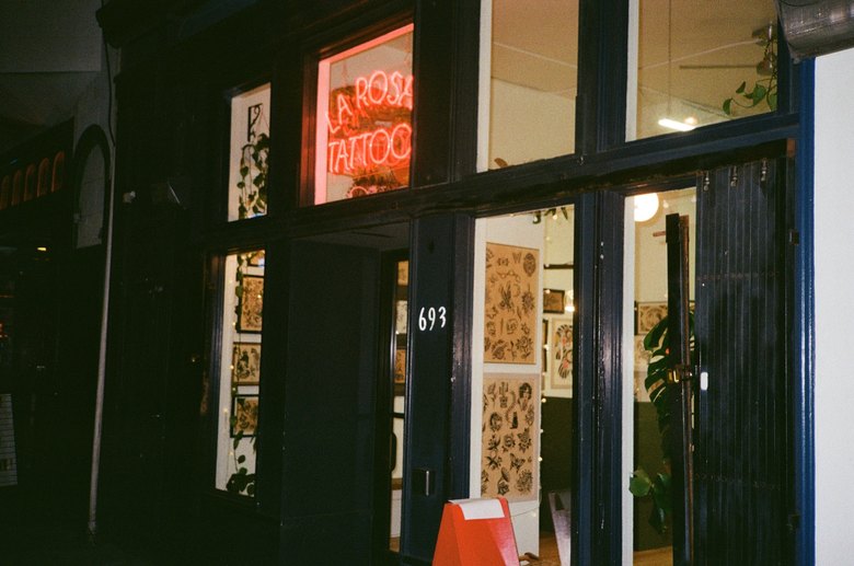 The La Rosa Tattoo storefront at night: red neon glowing in the window and the 693 door open.