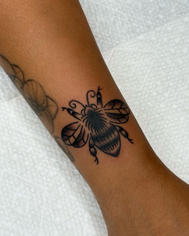A black and grey traditional bumblebee tattooed on the inside of a forearm.