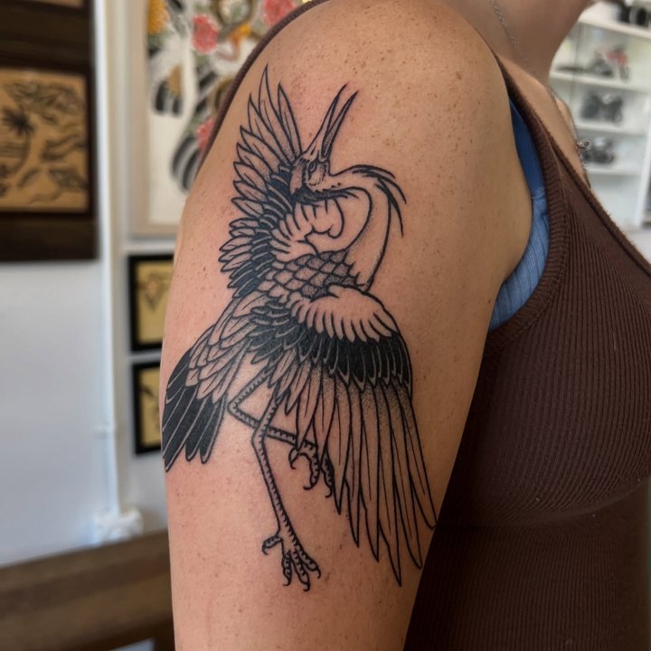 A black traditional heron with spread wings tattooed on an upper arm.