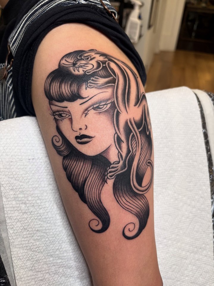 A black and grey traditional woman's head with a panther draped over it, tattooed on an arm.