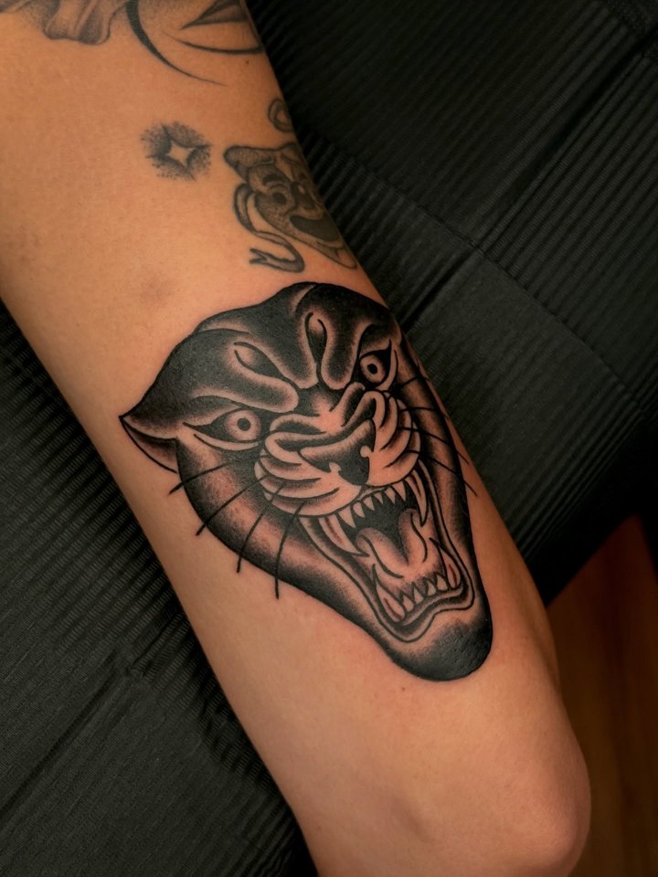 An American traditional roaring panther head tattooed on a forearm in black and grey.
