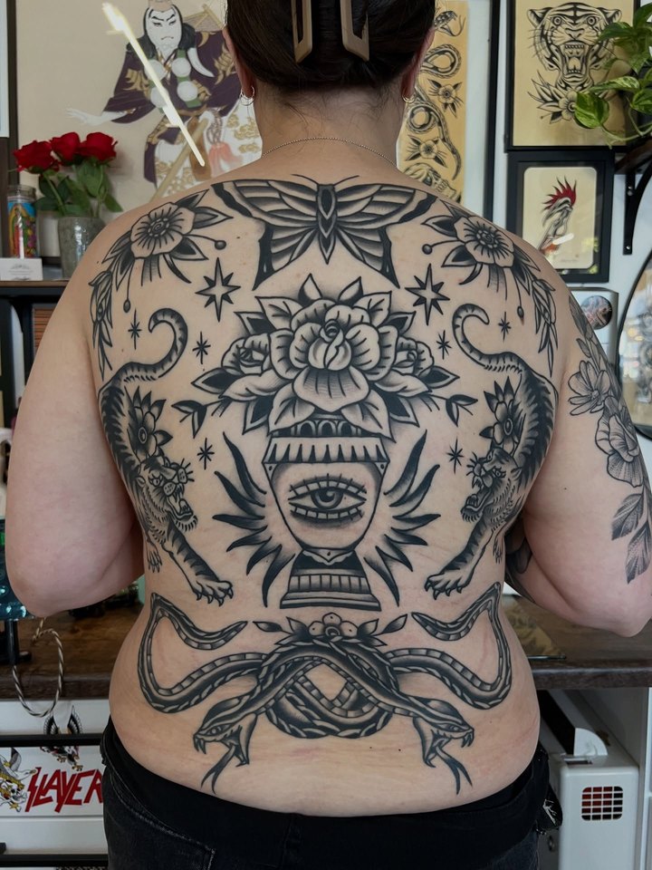 A full back piece in black and grey: a moth, twin crawling tigers, a rose urn with a radiant eye, and two crossed snakes at the base