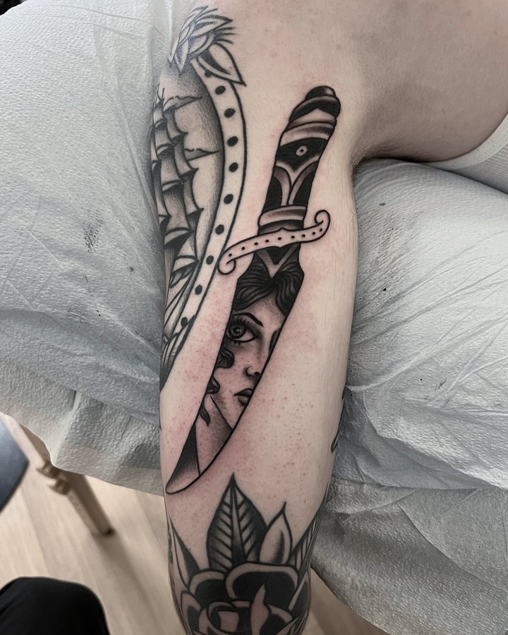 A dagger through a woman's head with a rose, tattooed on a calf