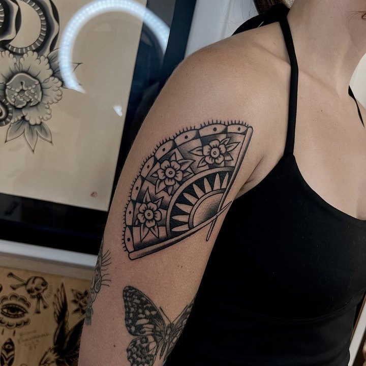 An ornamental folding fan with flowers and checkered panels tattooed on an upper arm