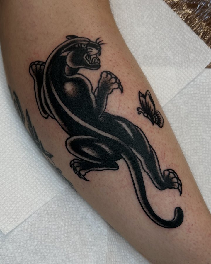 A crawling black panther with a small butterfly, tattooed on a forearm