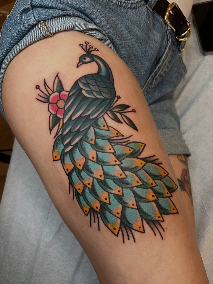 A full colour peacock with a teal tail tattooed along an upper arm