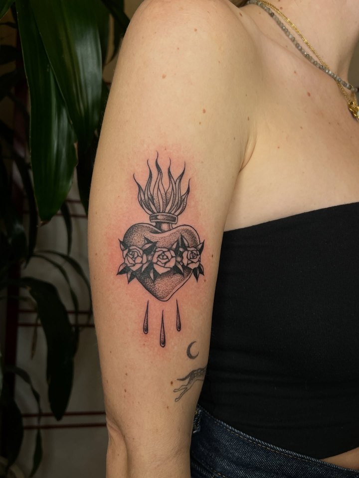 A black and grey sacred heart with flames and roses tattooed on an upper arm.