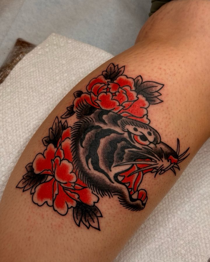 A Japanese traditional tiger head with red peonies tattooed on a lower leg.